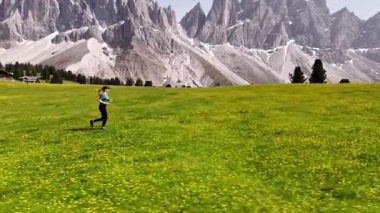 Kendini adamış bir koşucu hayat dolu ve yemyeşil bir çayırda nefes kesici bir Dolomitlere karşı ustalıkla yol alır.