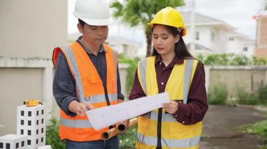 İnşaat mühendisi, müteahhit ve mimar inşaat alanında konuşuyor. Asyalı ustabaşı, inşaat sahasında planları tutuyor. Konut geliştirme projesi.