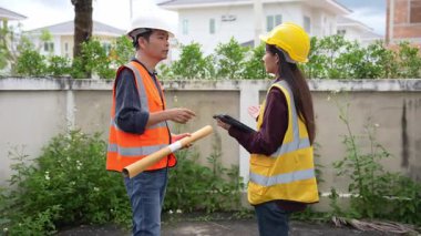 Asyalı kadın yatırımcı ve erkek mühendis köy inşaatı projesinde, gayrimenkul geliştirme projesinde ayakta durup konuşuyorlar..