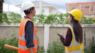 Asyalı kadın yatırımcı ve erkek mühendis köy inşaatı projesinde, gayrimenkul geliştirme projesinde ayakta durup konuşuyorlar..