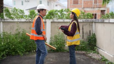 Asyalı kadın yatırımcı ve erkek mühendis köy inşaatı projesinde, gayrimenkul geliştirme projesinde ayakta durup konuşuyorlar..