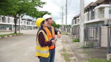 Bir projeyi inceleyen iki inşaat mühendisi, Asyalı bir kadın mimar ve bir erkek müteahhit, inşaat alanındaki bir binanın etrafında yürürken ellerinde tabletler ve panolar tutuyorlardı..