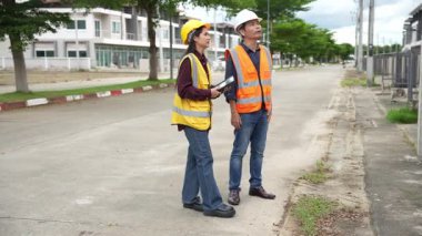 Bir projeyi inceleyen iki inşaat mühendisi, Asyalı bir kadın mimar ve bir erkek müteahhit, inşaat alanındaki bir binanın etrafında yürürken ellerinde tabletler ve panolar tutuyorlardı..