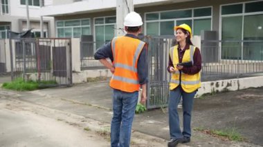 Bir projeyi inceleyen iki inşaat mühendisi, Asyalı bir kadın mimar ve bir erkek müteahhit, inşaat alanındaki bir binanın etrafında yürürken ellerinde tabletler ve panolar tutuyorlardı..