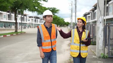 Bir projeyi inceleyen iki inşaat mühendisi, Asyalı bir kadın mimar ve bir erkek müteahhit, inşaat alanındaki bir binanın etrafında yürürken ellerinde tabletler ve panolar tutuyorlardı..