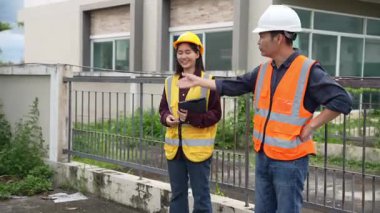 Bir projeyi inceleyen iki inşaat mühendisi, Asyalı bir kadın mimar ve bir erkek müteahhit, inşaat alanındaki bir binanın etrafında yürürken ellerinde tabletler ve panolar tutuyorlardı..