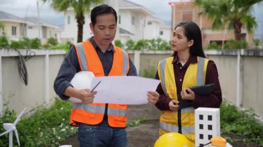 İnşaat mühendisi, müteahhit ve mimar inşaat alanında konuşuyor. Asyalı ustabaşı, inşaat sahasında planları tutuyor. Konut geliştirme projesi.