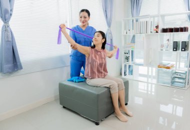 Asyalı fizyoterapist hastanın yatakta elastik bantla egzersiz yapmasına yardım ediyor. Klinikte orta yaşlı Asyalı kadınların elastik bantla egzersiz yapmasına yardım etmek..