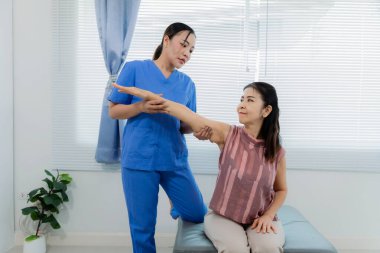 Rehabilitasyon, esneme, genç Asyalı hemşire orta yaşlı bir kadın hastaya kanepede fizik tedavi ve kas terapisi için yardım ediyor..
