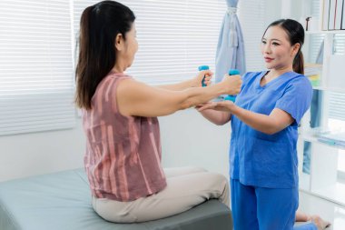 Rehabilitasyon, esneme, genç Asyalı hemşire orta yaşlı bir kadın hastaya kanepede fizik tedavi ve kas terapisi için yardım ediyor..