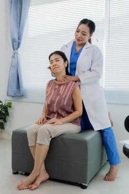Asyalı kadın doktor, boyun ve omuz ağrısı olan yaşlı kadın hastayı muayene ediyor. Doktor, koltukta zevkle oturan yaşlı bir Asyalı kadının omuzlarını ve kollarını muayene ediyor..