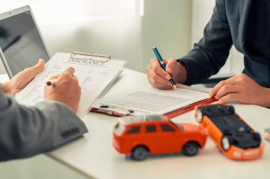A small toy car model sits next to stacks of insurance documents, a calculator, and a pen on an office desk. Close-up.