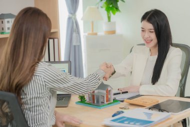 Asian female real estate agent and client shaking hands after signing home purchase contract approved. Buyer after property purchase is completed. Contract. Real estate.