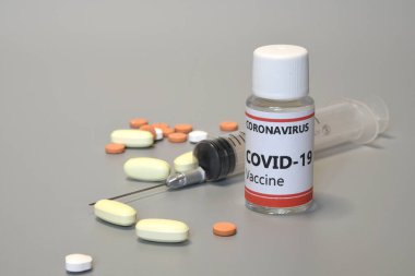 İçinde Covid-19 virüs aşısı ve gri arka planda izole edilmiş ilaç hapları bulunan bir şırınganın detayları. Coronavirus 'a karşı ilaç araştırması, konsept.