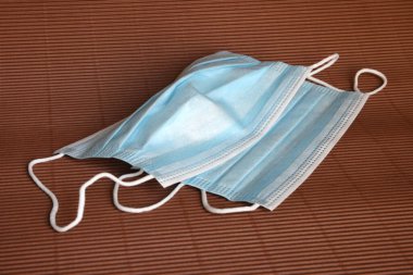 Koronavirüse karşı korunmak için antiviral mavi tıbbi maske. Kahverengi arka planda cerrahi koruyucu maske. Virüs ve salgın COVID-19 'un yayılmasının önlenmesi.