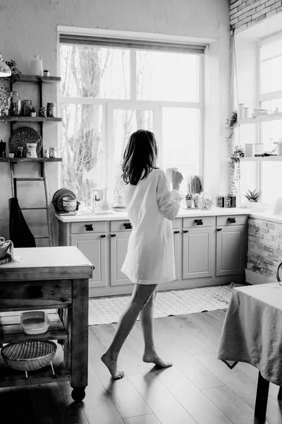 Femme réussie et confiante lors d'une pause café matinale, se reposer et profiter de la boisson. Jeune fille en culotte blanche et chemise longue avec épaule nue et poitrine debout sur la cuisine de la maison — Photo