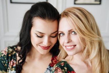 Sarışın ve esmer desenleri ile kısa yeşil elbiseler. Beyaz bir stüdyoda iki güzel kız.