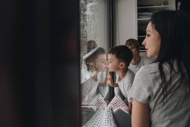 Aile pencerede oturuyor ve kış ormanına bakıyor. İyi yeni yıl ruhu. Pijamalı sabah.