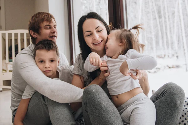 La famille est assise à la fenêtre et regarde la forêt d'hiver. Bon esprit du Nouvel An. Matin en pyjama . — Photo