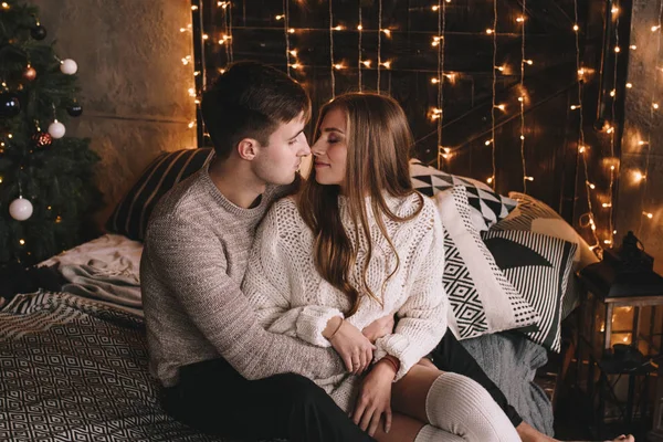 Un par en la cama del dormitorio. Interior oscuro. Año Nuevo y Navidad. Abrazos y besos. Amor. Jersey blanco y calcetines altos. Reunión romántica. Amantes de las citas. — Foto de Stock