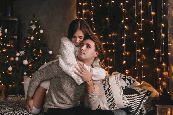 Un par en la cama del dormitorio. Interior oscuro. Año Nuevo y Navidad. Abrazos y besos. Amor. Jersey blanco y calcetines altos. Reunión romántica. Amantes de las citas. — Foto de Stock