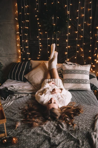 Un par en la cama del dormitorio. Interior oscuro. Año Nuevo y Navidad. Abrazos y besos. Amor. Jersey blanco y calcetines altos. Reunión romántica. Amantes de las citas. — Foto de Stock