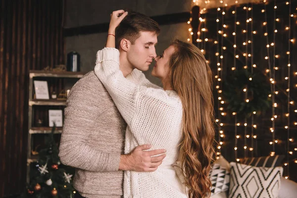 Paar auf dem Bett im Schlafzimmer. Dunkles Interieur. Neujahr und Weihnachten. Umarmungen und Küsse. Liebe. Weißer Pullover und hohe Socken. Romantisches Treffen. Ein Date. — Stockfoto