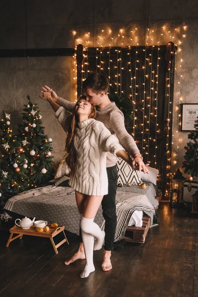 Paar auf dem Bett im Schlafzimmer. Dunkles Interieur. Neujahr und Weihnachten. Umarmungen und Küsse. Liebe. Weißer Pullover und hohe Socken. Romantisches Treffen. Ein Date. — Stockfoto