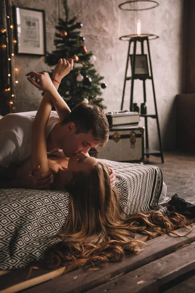 Paar auf dem Bett im Schlafzimmer. Dunkles Interieur. Neujahr und Weihnachten. Umarmungen und Küsse. Liebe. Weißer Pullover und hohe Socken. Romantisches Treffen. Ein Date. — Stockfoto