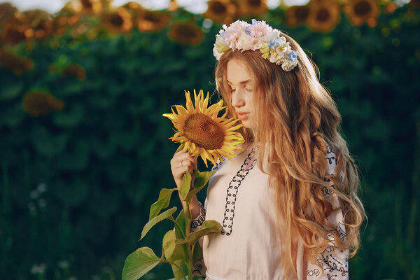 Young and beautiful girl dressed in national Ukrainian costumes standing near sunflowers in the field