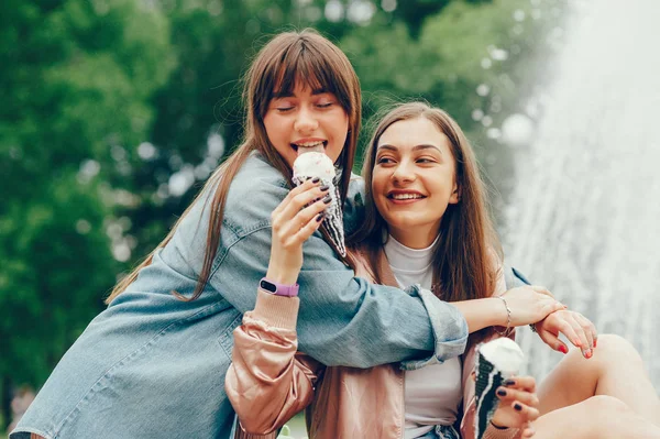 Dos chicas sentadas cerca de la fuente y comiendo helado . — Foto de Stock