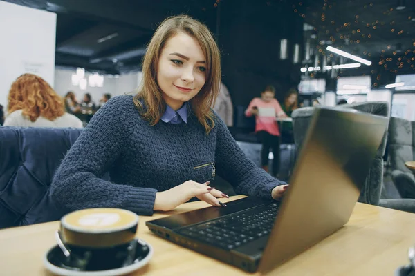 美しい少女は コンピューター付きのカフェに座っているし コーヒーを飲む — ストック写真