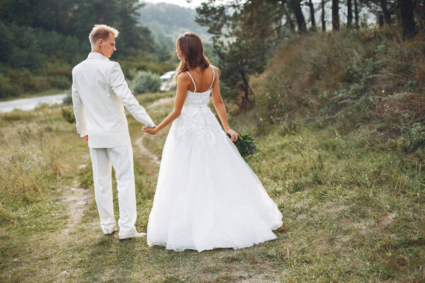 Beautiful bride in a white dress. Couple in a summer field. Woman with a bouquet of flowers