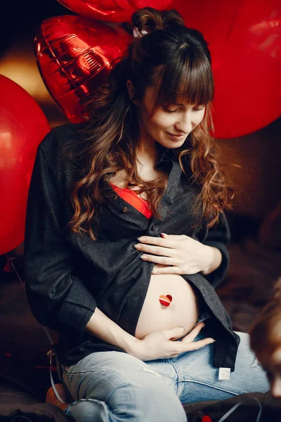 Zwangere vrouw in een leuke jurk zittend op een bed — Stockfoto