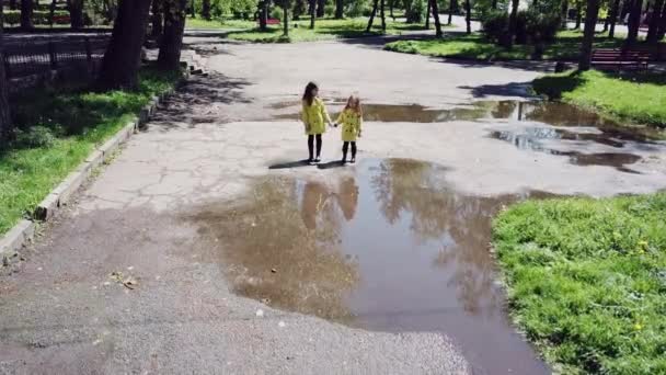 Duas meninas brincando e correndo através de poças no parque — Vídeo de Stock