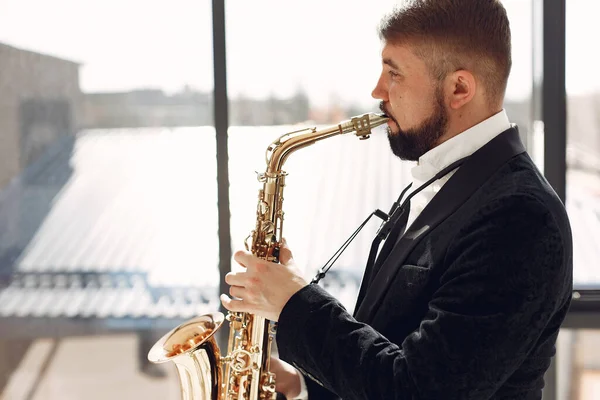 Man in black suit standing with a saxophone