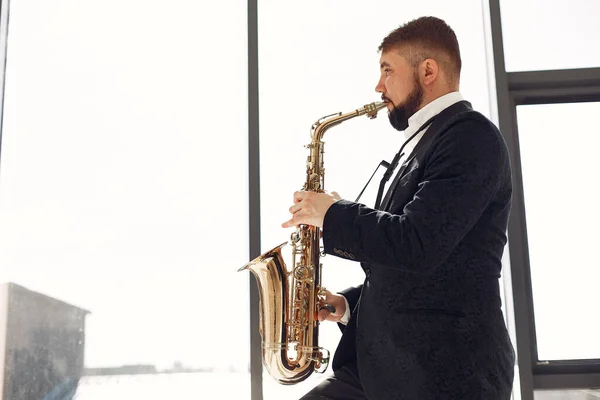Man in black suit standing with a saxophone