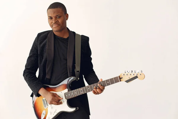 Black man in black suit standing with a guitar