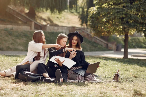 Tre studenter sitter på et gress med en bærbar datamaskin – stockfoto