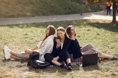 Three students sitting on a grass with laptop clipart