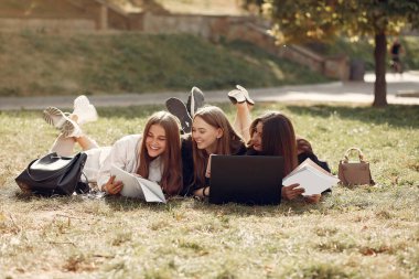 Three students sitting on a grass with laptop clipart