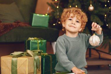 Gri kazaklı küçük çocuk Noel ağacının yanında