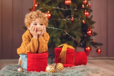 Küçük çocuk Noel ağacının yanında kahverengi kazaklı.