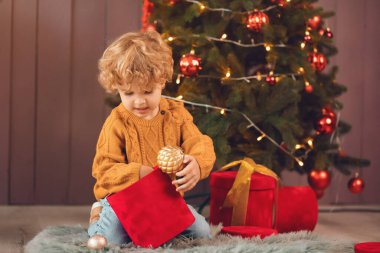 Küçük çocuk Noel ağacının yanında kahverengi kazaklı.