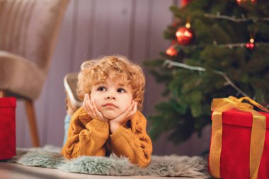 Küçük çocuk Noel ağacının yanında kahverengi kazaklı.