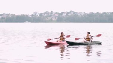 İki kadın arkadaş gölde kayak yapıyor.