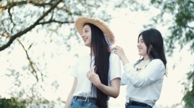 İki kız arkadaş, biri göl kenarında hasır şapka takıyor ve gülümsüyor.