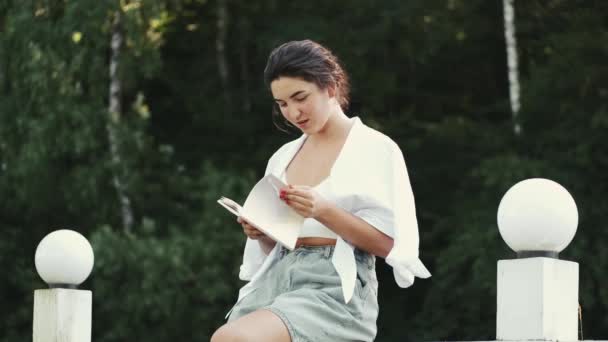 푸른 공원에서 미소짓고 책을 읽는 젊은 여자 — 비디오