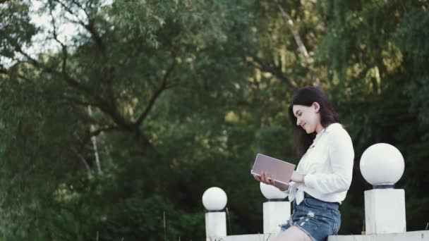 Молодая красивая женщина улыбается и читает книгу в зеленом парке — стоковое видео