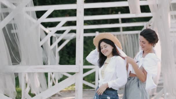Two girlfriends, one wearing a straw hat at the arbor smiling — Stock Video